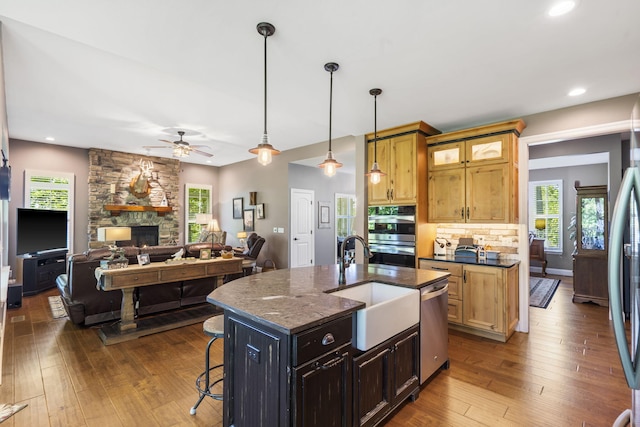 103 Dogwood Ct, Saddlebrooke, MO 65630 - kitchen featuring appliances with stainless steel finishes, a fireplace, a sink, ceiling fan, and dark wood-style floors