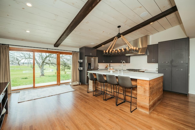 5724 E Mill St, Springfield, MO 65802 - kitchen with wall chimney range hood, light countertops, a kitchen bar, high end fridge, and light wood-type flooring