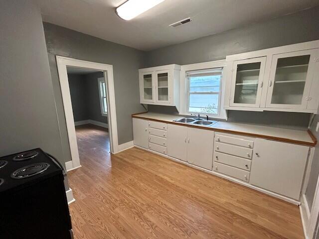2238 N Rogers Ave, Springfield, MO 65803 - kitchen with black electric range, a sink, white cabinets, light wood-style flooring, and glass insert cabinets
