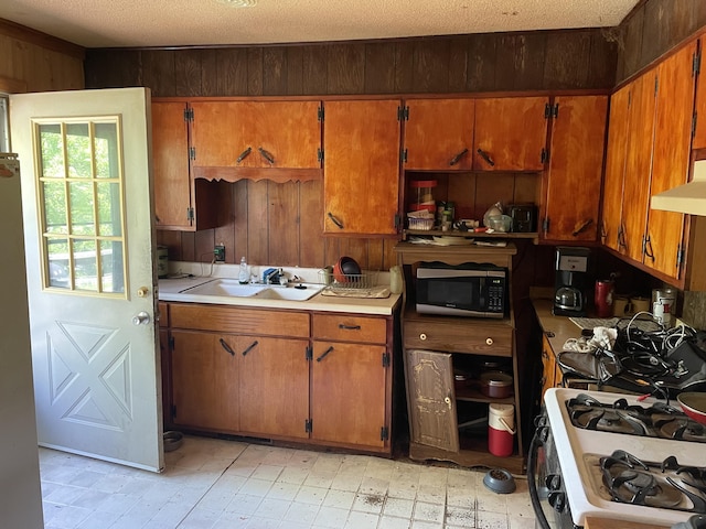 kitchen with stainless steel microwave, white gas range, a sink, wooden walls, and light countertops