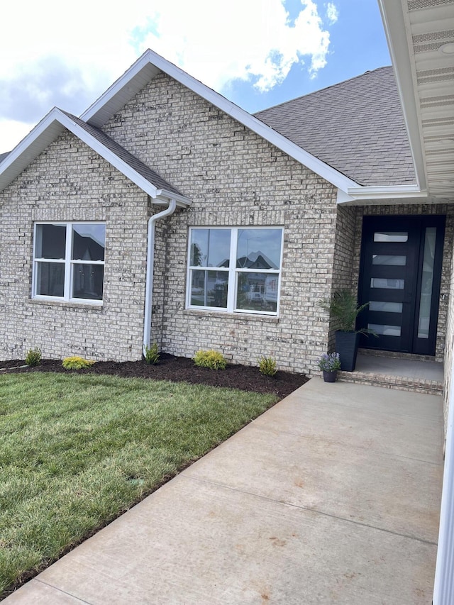 2077 N Sun Valley Dr, Springfield, MO 65802 - doorway to property featuring roof with shingles, a yard, and brick siding