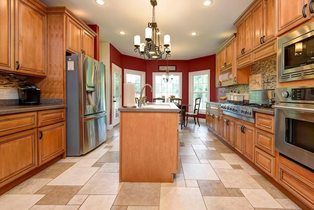 kitchen with appliances with stainless steel finishes, a chandelier, an island with sink, brown cabinets, and recessed lighting