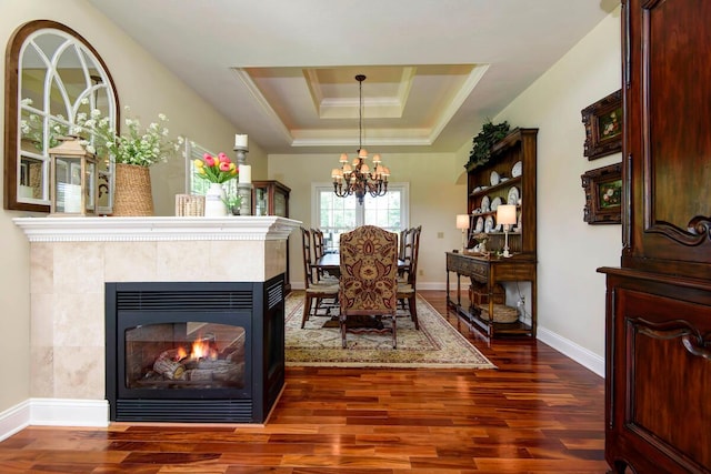 dining area with dark wood-style flooring, a chandelier, a multi sided fireplace, baseboards, and a tray ceiling