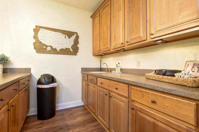 kitchen with a sink, baseboards, dark wood-style floors, and brown cabinetry