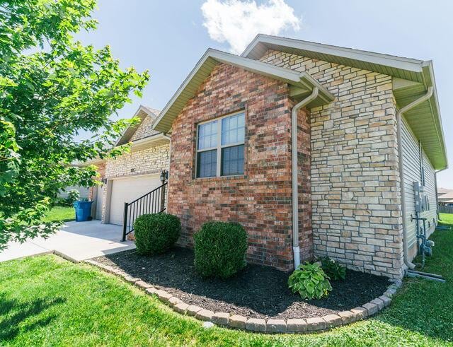 1205 N 12th Ave, Ozark, MO 65721 - view of home's exterior with a garage, a lawn, brick siding, stone siding, and concrete driveway