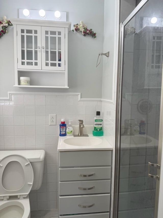full bath with tile walls, toilet, a stall shower, vanity, and wainscoting