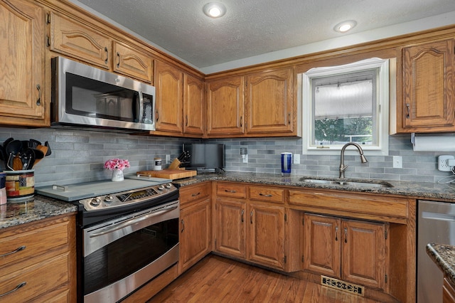 2019 N Preakness Dr, Nixa, MO 65714 - kitchen featuring appliances with stainless steel finishes, a sink, brown cabinetry, dark stone counters, and light wood-style flooring
