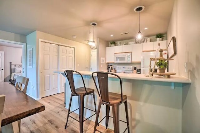 120 Spring Creek Ct Unit 12, Branson, MO 65616 - kitchen featuring white appliances, a kitchen breakfast bar, light wood-type flooring, decorative light fixtures, and white cabinetry