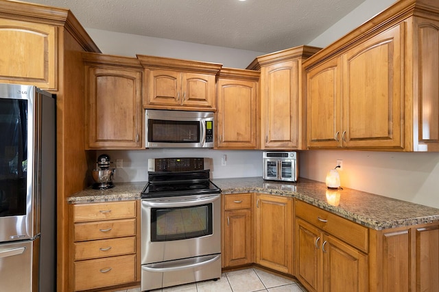 2310 Lakeside Ct, Ozark, MO 65721 - kitchen featuring stainless steel appliances, brown cabinetry, light tile patterned floors, and dark stone counters