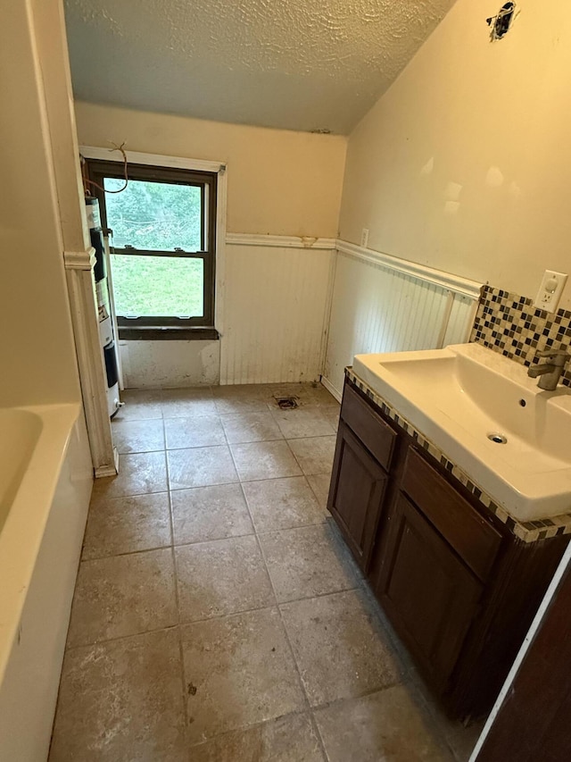 911 W Locust St, Springfield, MO 65803 - full bath with a textured ceiling, wainscoting, tile patterned floors, vanity, and a tub