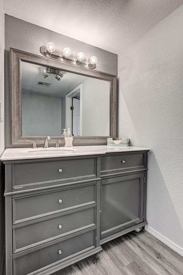 511 N E, Columbus, KS 66725 - bathroom with a textured wall, wood finished floors, baseboards, vanity, and a textured ceiling