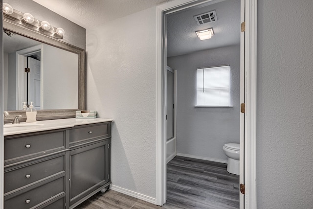 511 N E, Columbus, KS 66725 - bathroom featuring wood finished floors, toilet, vanity, baseboards, and a textured wall