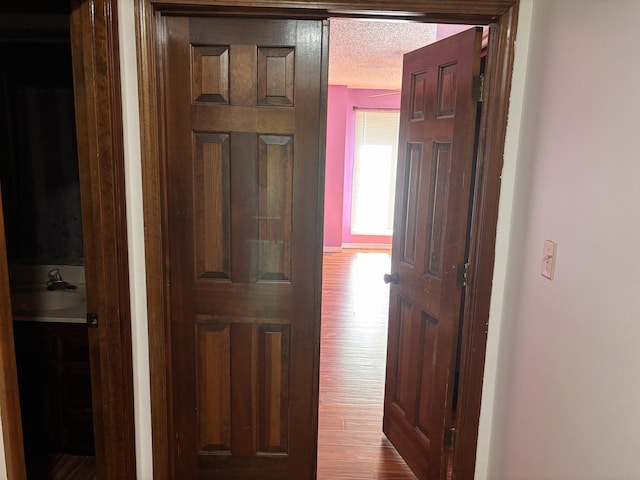 hall featuring a sink, wood finished floors, and a textured ceiling