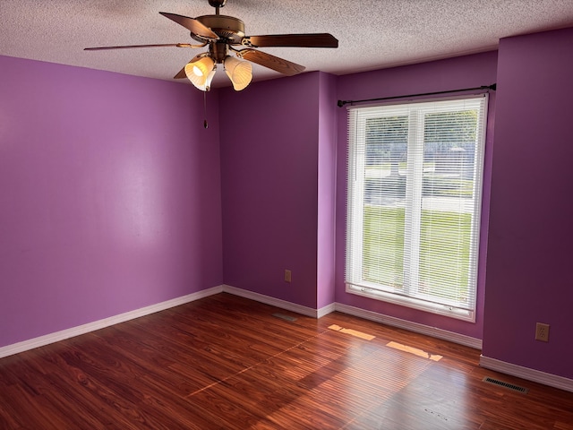 unfurnished room featuring plenty of natural light, ceiling fan, a textured ceiling, wood finished floors, and baseboards