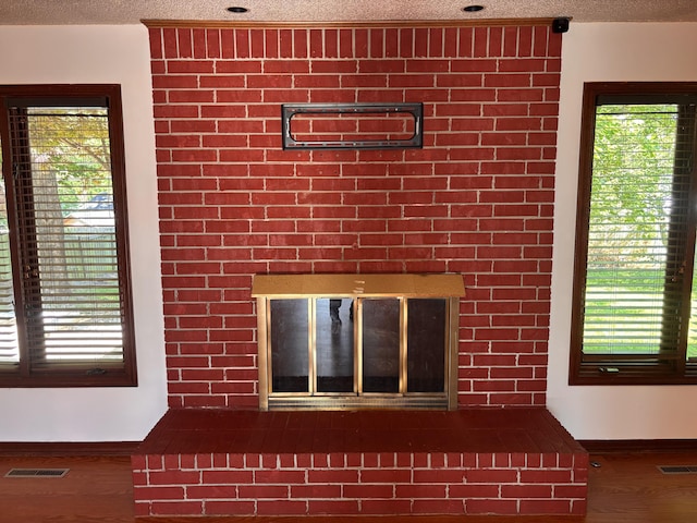 detailed view of wood finished floors, baseboards, a glass covered fireplace, and a textured ceiling