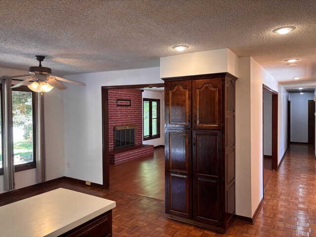 kitchen featuring baseboards, a textured ceiling, a ceiling fan, dark brown cabinets, and a fireplace