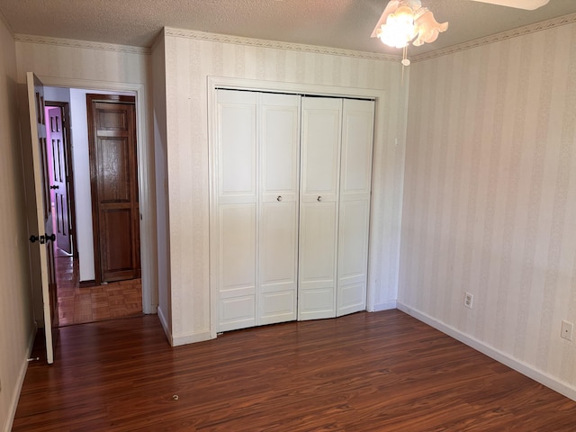 unfurnished bedroom featuring dark wood-style flooring, wallpapered walls, baseboards, a closet, and a textured ceiling