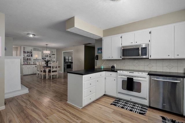 1511 E University St, Springfield, MO 65804 - kitchen with stainless steel appliances, a peninsula, dark countertops, a chandelier, and light wood-type flooring