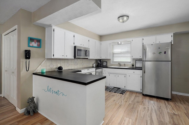 1511 E University St, Springfield, MO 65804 - kitchen featuring appliances with stainless steel finishes, dark countertops, light wood finished floors, tasteful backsplash, and a peninsula