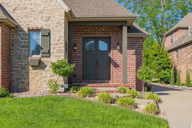 853 E Grafton Dr, Nixa, MO 65714 - view of exterior entry with brick siding, a shingled roof, a lawn, and driveway