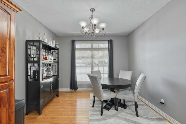 3192 W Melbourne St, Springfield, MO 65810 - dining room featuring a chandelier, light wood-style flooring, a bar, baseboards, and a textured ceiling
