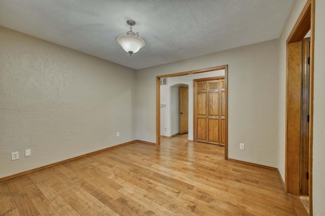224 Loveland Dr, Rogersville, MO 65742 - unfurnished bedroom featuring a textured wall, light wood-style flooring, baseboards, arched walkways, and a textured ceiling