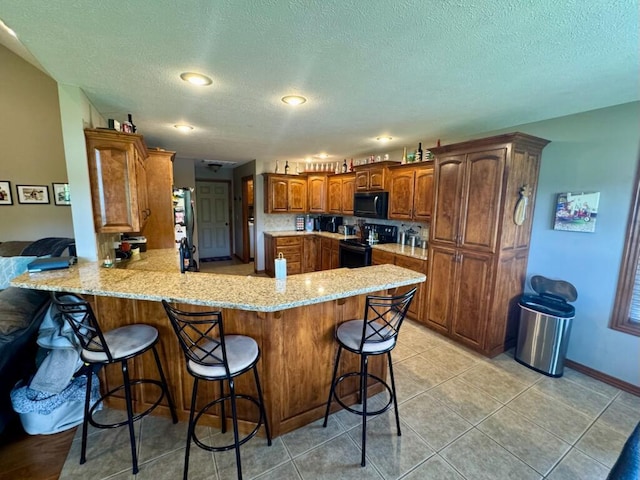 1054 W Itaska Rd, Nixa, MO 65714 - kitchen featuring black appliances, a peninsula, a kitchen bar, a textured ceiling, and light stone counters
