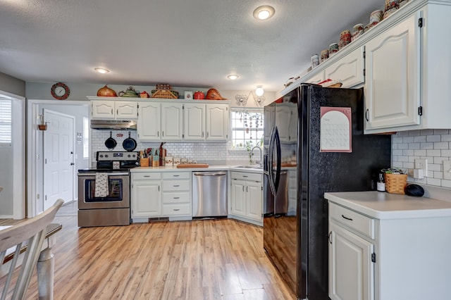 307 Azalea St, Duenweg, MO 64841 - kitchen featuring appliances with stainless steel finishes, under cabinet range hood, decorative backsplash, light wood-type flooring, and white cabinetry