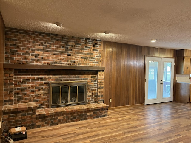 641 N Claud Ave, Bolivar, MO 65613 - unfurnished living room featuring a textured ceiling, wood finished floors, wooden walls, a brick fireplace, and french doors