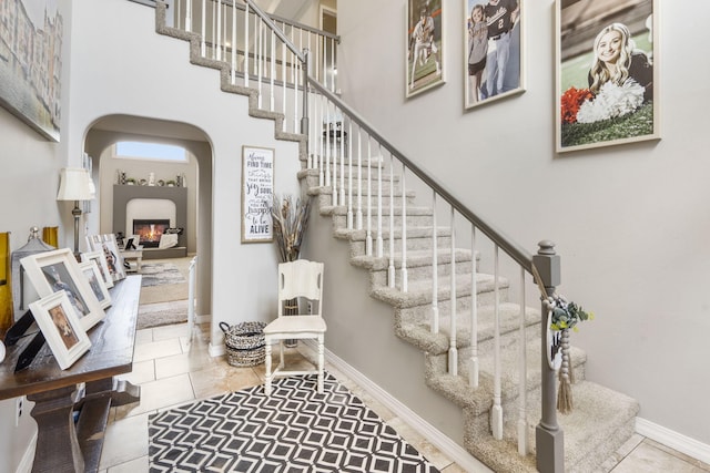 3909 W Eaglecrest St, Battlefield, MO 65619 - stairs featuring arched walkways, a high ceiling, tile patterned floors, a glass covered fireplace, and baseboards