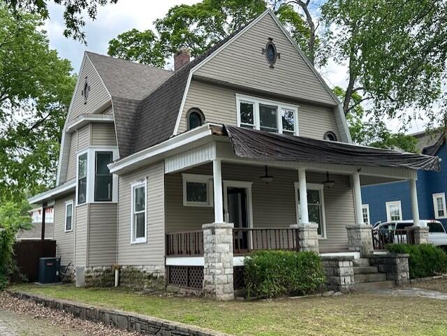 1052 S Garrison Ave, Carthage, MO 64836 - colonial inspired home with a gambrel roof, a porch, central air condition unit, a shingled roof, and a chimney
