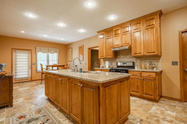 8326 Shinnecock Dr, Nixa, MO 65714 - kitchen featuring gas stove, under cabinet range hood, brown cabinetry, a sink, and a kitchen island with sink