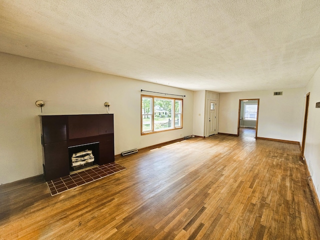 107 W Poplar St, El Dorado Springs, MO 64744 - unfurnished living room with a textured ceiling, wood finished floors, healthy amount of natural light, a tile fireplace, and baseboards