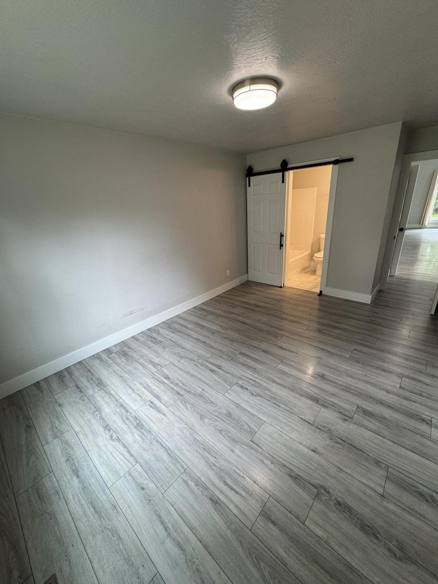 108 Jasper St, Aurora, MO 65605 - unfurnished bedroom featuring a barn door, baseboards, wood finished floors, a textured ceiling, and ensuite bath