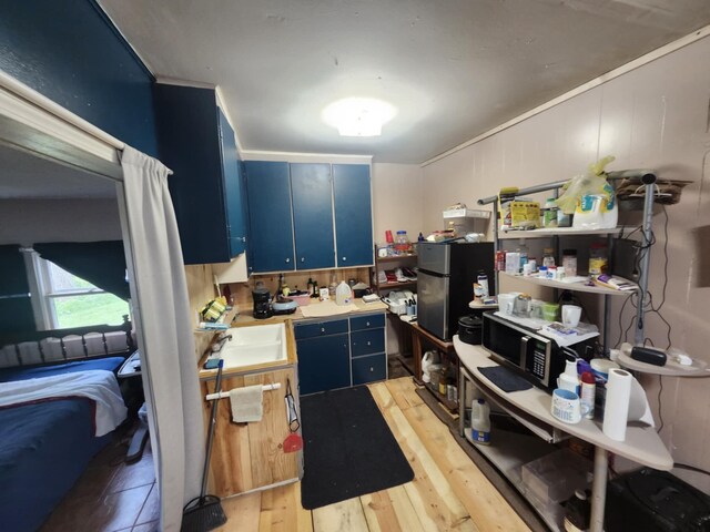 626 W N St, Mountain Grove, MO 65711 - kitchen featuring blue cabinetry, stainless steel appliances, light wood finished floors, a sink, and light countertops