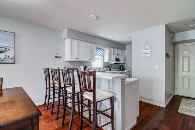 123 Bunker Ridge Dr Unit 4, Branson, MO 65616 - kitchen with white microwave, a kitchen bar, dark wood-style flooring, white cabinets, and a peninsula
