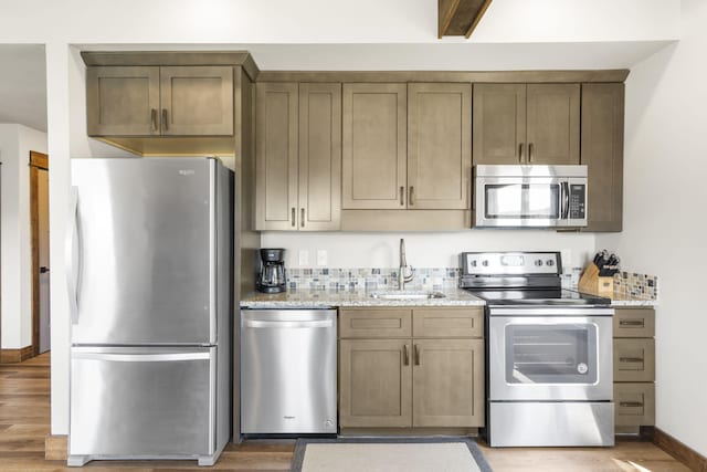 kitchen with appliances with stainless steel finishes, a sink, light wood-style flooring, light stone counters, and baseboards