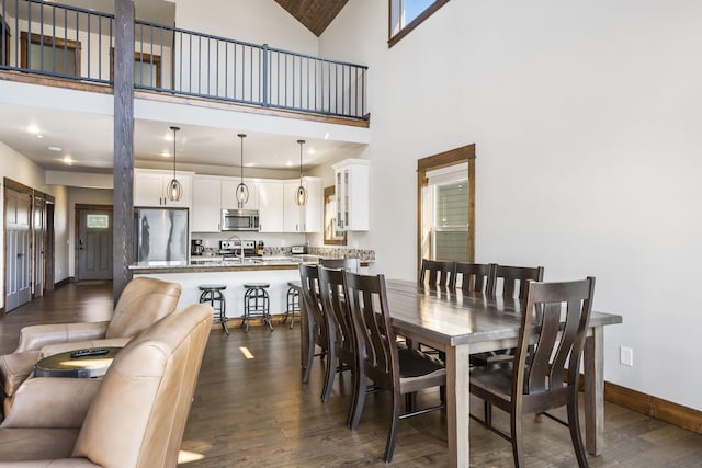 dining space featuring dark wood-style floors, a high ceiling, and baseboards