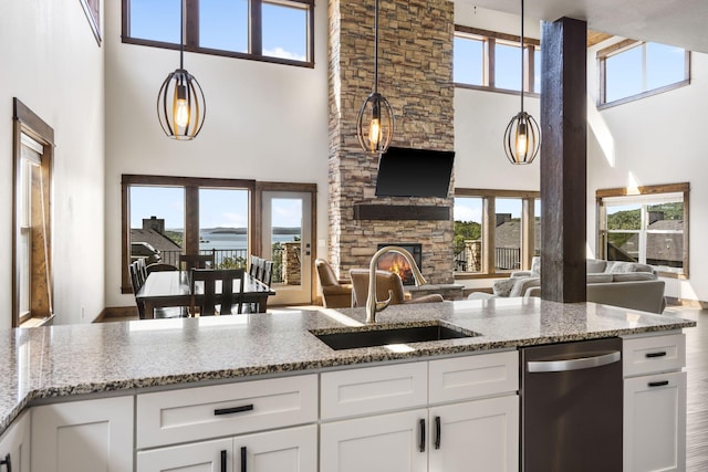 kitchen featuring a towering ceiling, stainless steel dishwasher, a sink, open floor plan, and white cabinetry