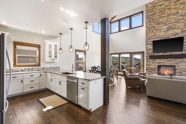 kitchen featuring stainless steel appliances, a peninsula, a sink, open floor plan, and light stone counters