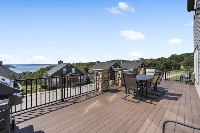wooden terrace featuring outdoor dining space, grilling area, and a water view