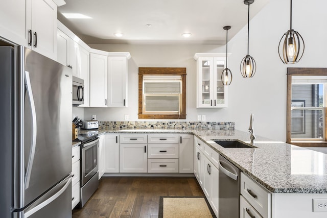 kitchen featuring stainless steel appliances, a sink, a peninsula, white cabinets, and glass insert cabinets