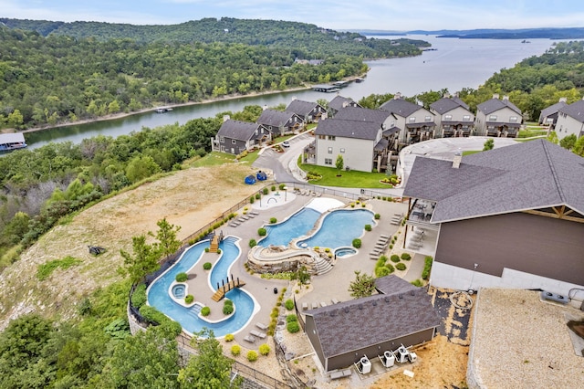 aerial view of residential area featuring a nearby body of water, a pool, and a heavily wooded area