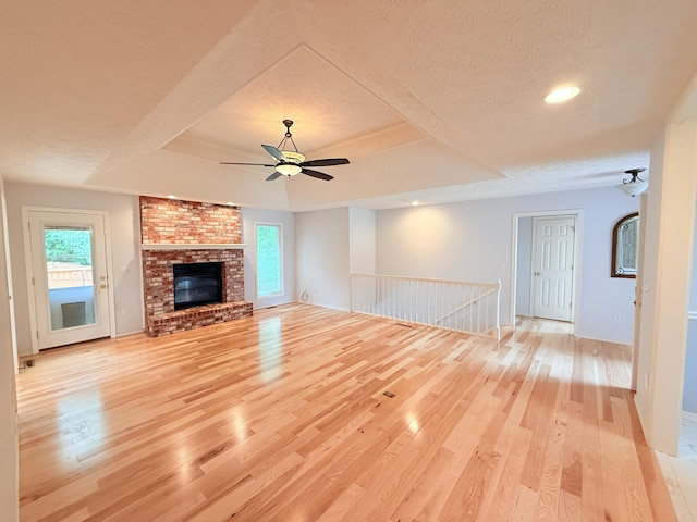 5135 S Clay Ave, Springfield, MO 65810 - unfurnished living room featuring light wood-style flooring, plenty of natural light, a textured ceiling, a ceiling fan, and a brick fireplace