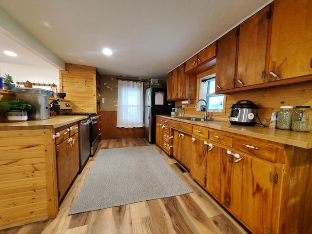 1010 Pine St, Cabool, MO 65689 - kitchen with gas range, light wood-type flooring, wood walls, freestanding refrigerator, and a sink