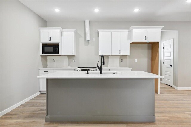 1239 W Arlington Ct, Springfield, MO 65803 - kitchen featuring black microwave, white cabinetry, a center island with sink, light countertops, and baseboards