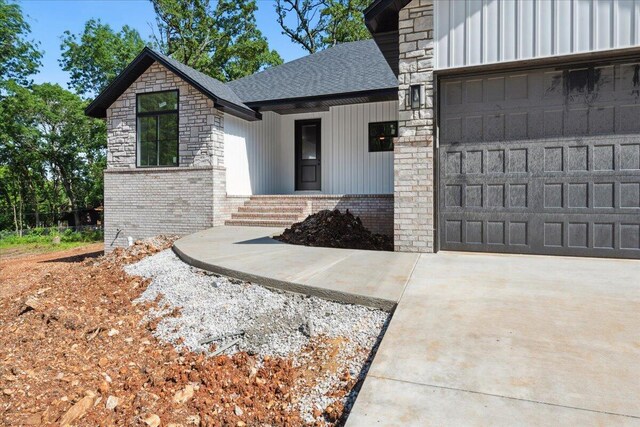 1239 W Arlington Ct, Springfield, MO 65803 - view of exterior entry with brick siding, a shingled roof, a garage, driveway, and board and batten siding