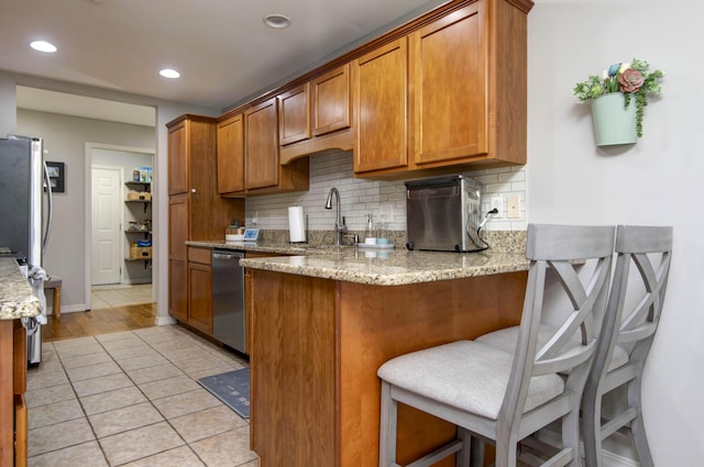 326 Country Bluff Dr, Branson, MO 65616 - kitchen with appliances with stainless steel finishes, decorative backsplash, brown cabinetry, a peninsula, and light stone counters
