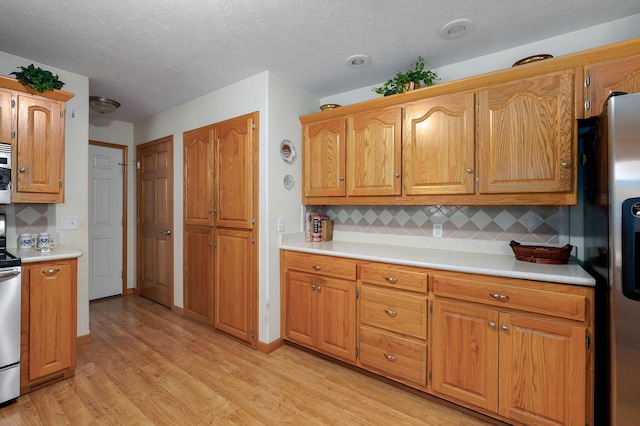 5473 N State Highway 125, Strafford, MO 65757 - kitchen featuring light wood-style flooring, light countertops, decorative backsplash, appliances with stainless steel finishes, and a textured ceiling