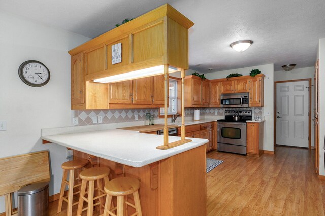 5473 N State Highway 125, Strafford, MO 65757 - kitchen featuring appliances with stainless steel finishes, decorative backsplash, a peninsula, light countertops, and a kitchen bar